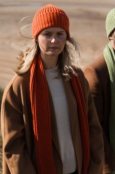 a woman in an orange hat and scarf standing next to a man wearing a brown coat