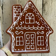 a hand holding up a brown and white gingerbread house cookie