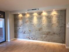 an empty room with wood flooring and stone wall behind the door is illuminated by recessed lights