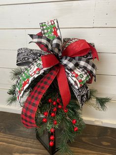 a christmas wreath on top of a black stand with red and white ribbons, pine cones and berries