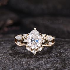 an engagement ring with a pear shaped diamond surrounded by smaller round diamonds on a rock