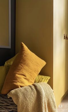 a basket filled with yellow and brown pillows next to a wall in a living room