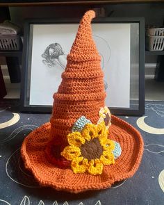 a crocheted hat with a sunflower on it sitting next to a framed photo