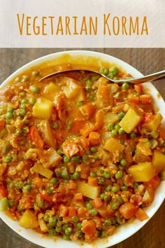 a white bowl filled with vegetable korma next to a spoon on top of a wooden table