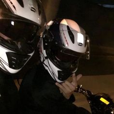 two people wearing helmets are sitting next to each other on a motorcycle at night time