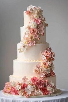 a three tiered wedding cake with pink and white flowers on the top, sitting on a table