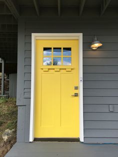 a yellow door on a gray house with two lights and a light fixture above it