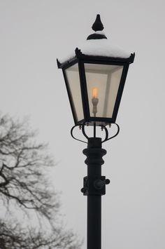 an old fashioned street light with snow on top and trees in the backgroud