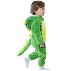 a young boy in a green dinosaur costume is walking with his foot on the ground