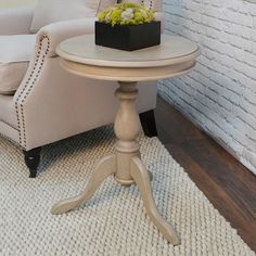 a chair and table in a room with white brick wall behind the couch, along with a potted plant on top