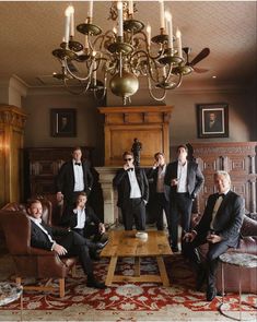 a group of men in tuxedos are sitting around a table with candles on it