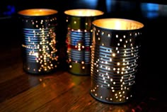 three tin cans with lights on them sitting on a wooden table next to each other