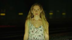 a woman with headphones standing in front of train tracks at night, looking off to the side