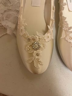 two pairs of white shoes with lace and pearls on the bottom one pair has a flower brooch