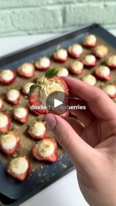 someone is holding up a strawberry with cream cheese on it in front of a tray of strawberries