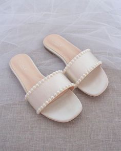 a pair of white shoes with pearls on the bottom and straps, sitting on top of a bed