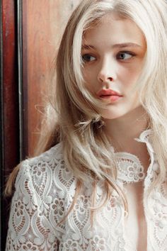 a woman with long blonde hair standing in front of a wooden door wearing a white blouse