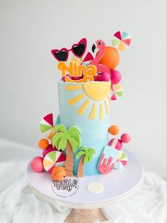 a colorful cake decorated with palm trees and beach decorations on a white tableclothed surface