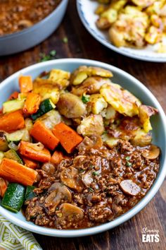 a bowl filled with meat and vegetables on top of a wooden table next to other dishes