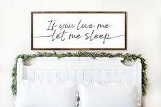 a bed with white pillows and a wooden sign above it that says if you love me let me sleep