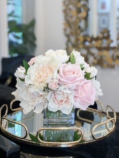 a vase filled with pink and white flowers on top of a glass table next to a mirror