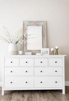 a white dresser with flowers and a mirror on it's top shelf in a room