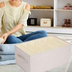 a woman sitting on the floor next to some folded clothes and a box with shoes in it