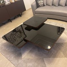 a glass coffee table sitting on top of a rug in front of a gray couch