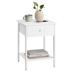 a white table with a book, coffee cup and plant on the shelf next to it