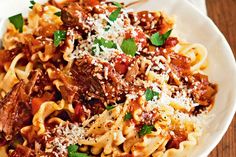 a white bowl filled with pasta and meat covered in sauce, parmesan cheese