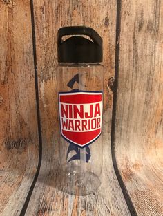 a glass water bottle with the words ninja warrior printed on it, sitting on a wooden surface