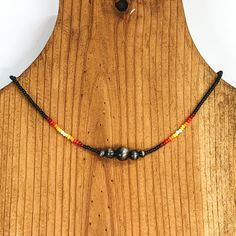 Black beaded necklace with center silver beads of varying sizes. On each side of the silver, center beads there is a segment the has white center beads with yellow, orange, red, and maroon beads folowing on each side. This necklace is pictured on a wooden necklace holder on a white background. Giddy Up Glamour, Strung Beads, Beaded Choker Necklace, Beaded Choker, Beading Patterns, Jewelry Ideas, Matching Earrings, Silver Beads, Bead Work