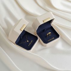 an open ring box with two rings inside on a white cloth covered bedding sheet