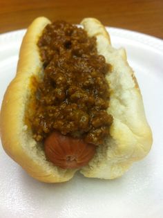 a hot dog with chili on it sitting on a paper plate