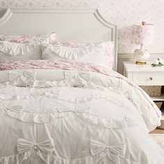 a white bed with pink and white comforter in a bedroom next to a night stand