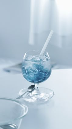 a glass filled with water sitting on top of a table next to a bowl and spoon