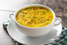 a bowl of soup with noodles and carrots on a saucer next to a napkin