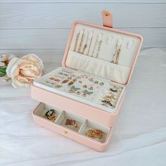 an open pink jewelry box sitting on top of a white table next to a flower