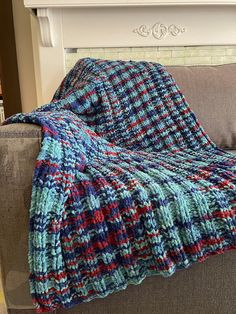 a blue and red blanket sitting on top of a gray couch next to a fire place