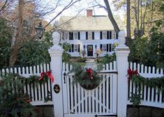 a white picket fence with wreaths and christmas decorations on the top, in front of a house