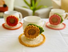 three crocheted coffee cups and saucers on a white tablecloth with flowers