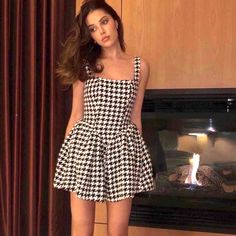 a woman standing in front of a fireplace wearing a black and white checkered dress