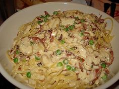 a white bowl filled with pasta covered in chicken and peas