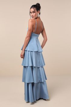 a woman wearing a blue dress with tiered layers and open back, looking at the camera