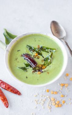 a white bowl filled with broccoli soup next to two spoons and corn