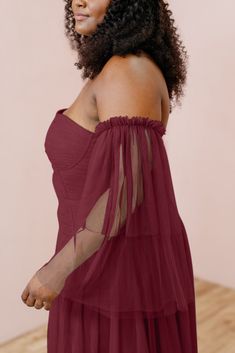 a woman with curly hair wearing a red dress and looking off to the side while standing in front of a pink wall