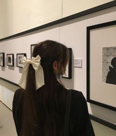 a woman with a bow in her hair looking at pictures on the wall