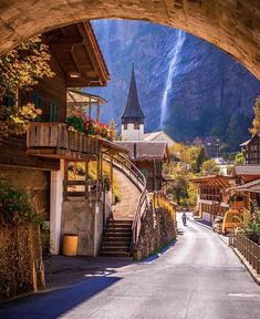 a person walking down a narrow street in front of a mountain side town with a waterfall coming out of it