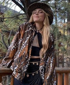 a woman standing next to a tree wearing a leopard print jacket and skirt with high heels