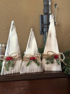 three white wooden christmas trees with red berries and greenery tied to them on a mantle